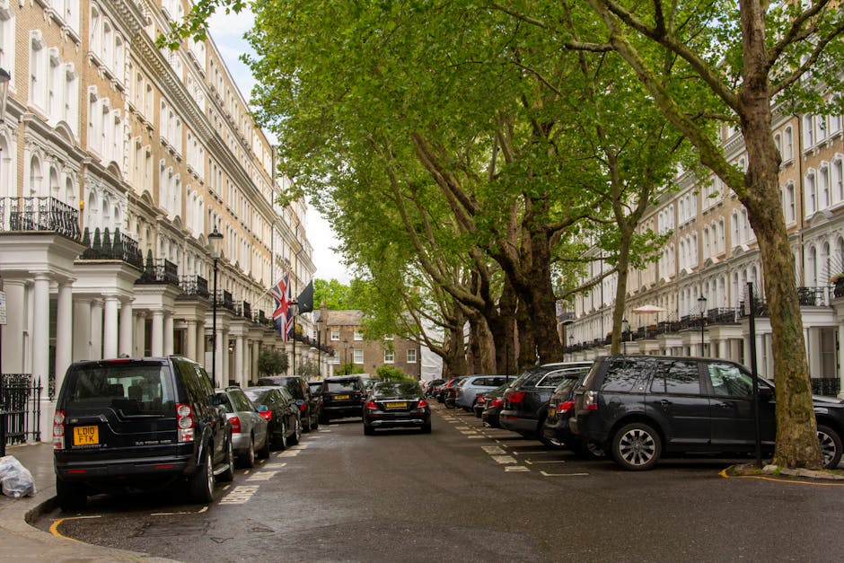 A row of elegant, multi-story Victorian-style townhouses in a residential area of St John's Wood, London, featuring white facades, decorative black wrought-iron balconies, and large sash windows. The